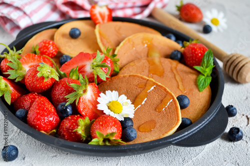 Pancakes with berries and honey in a pan on a concrete backgroun