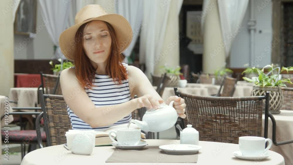 beautiful young girl in outdoor cafe reading a book and drinking tea. phone. student. business woman beautiful young girl in outdoor cafe reading a book and drinking tea. phone. student. business woman