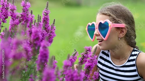 Beautiful girl in big glasses in the shape of hearts near purple flowers. Girl in big sunglasses smells flowers photo