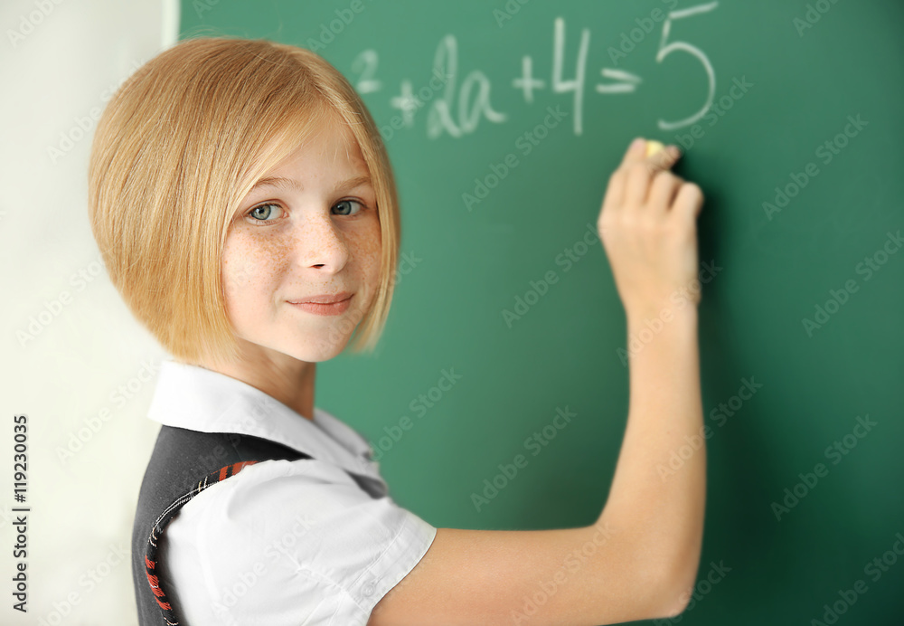 Cute schoolgirl writing on chalkboard