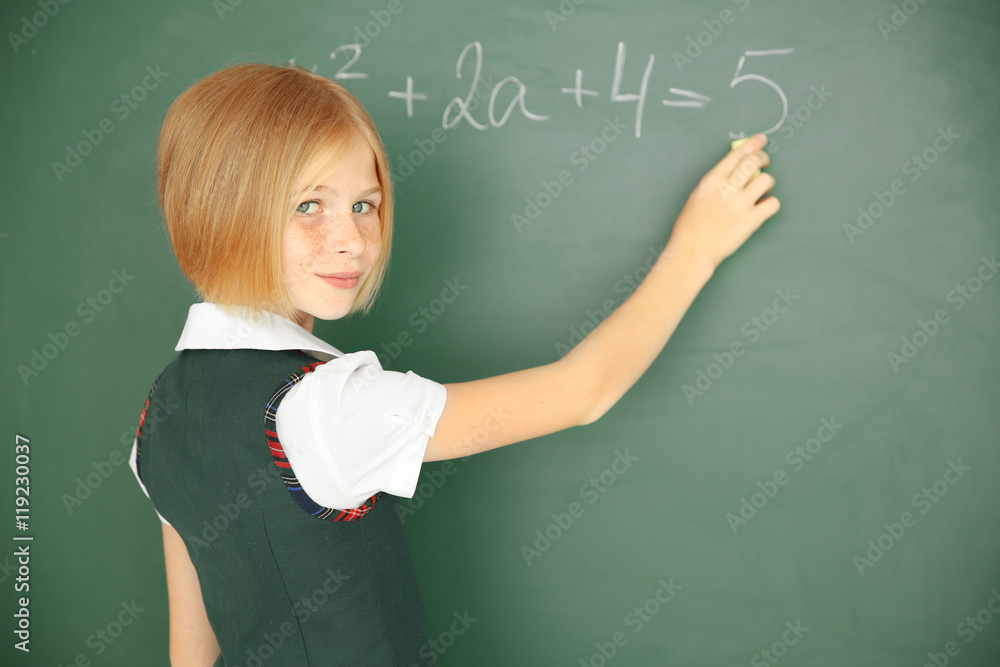 Cute schoolgirl writing on chalkboard