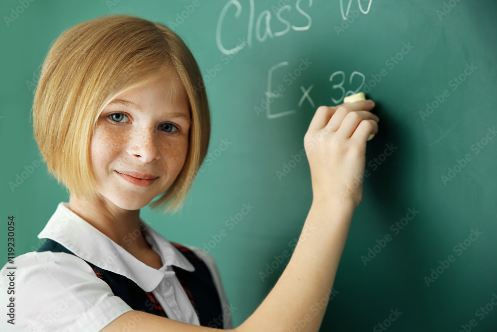 Cute schoolgirl writing on chalkboard