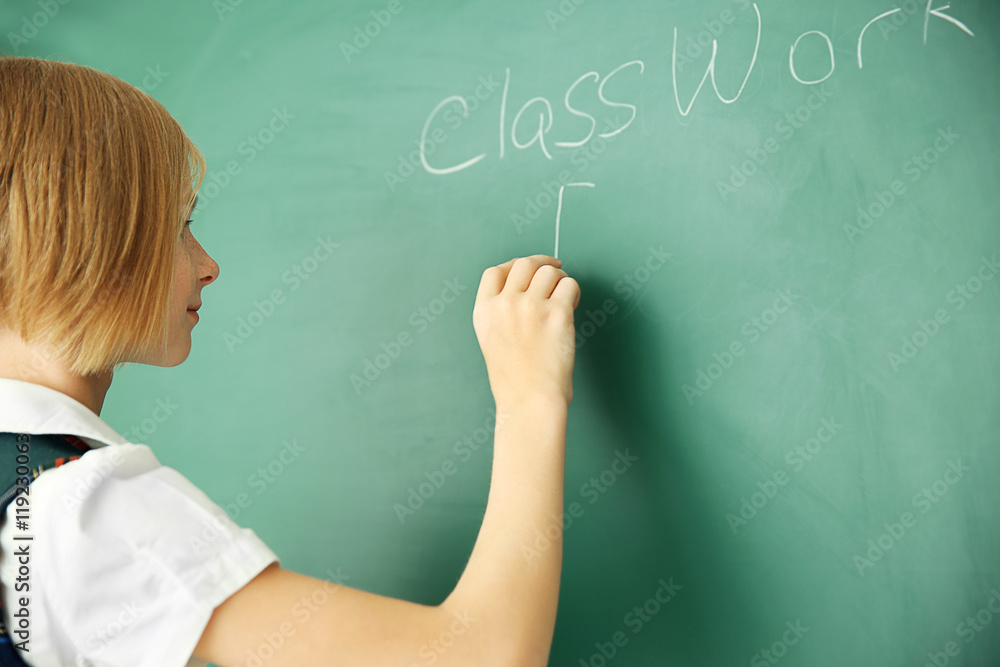 Cute schoolgirl writing on chalkboard