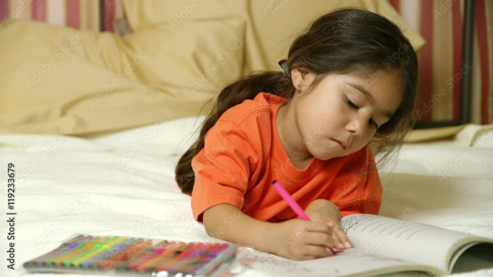 Lying on a bed a cute little girl of Hispanic heritage colors quietly in her coloring book. Lying on a bed a cute little girl of Hispanic heritage colors quietly in her coloring book.