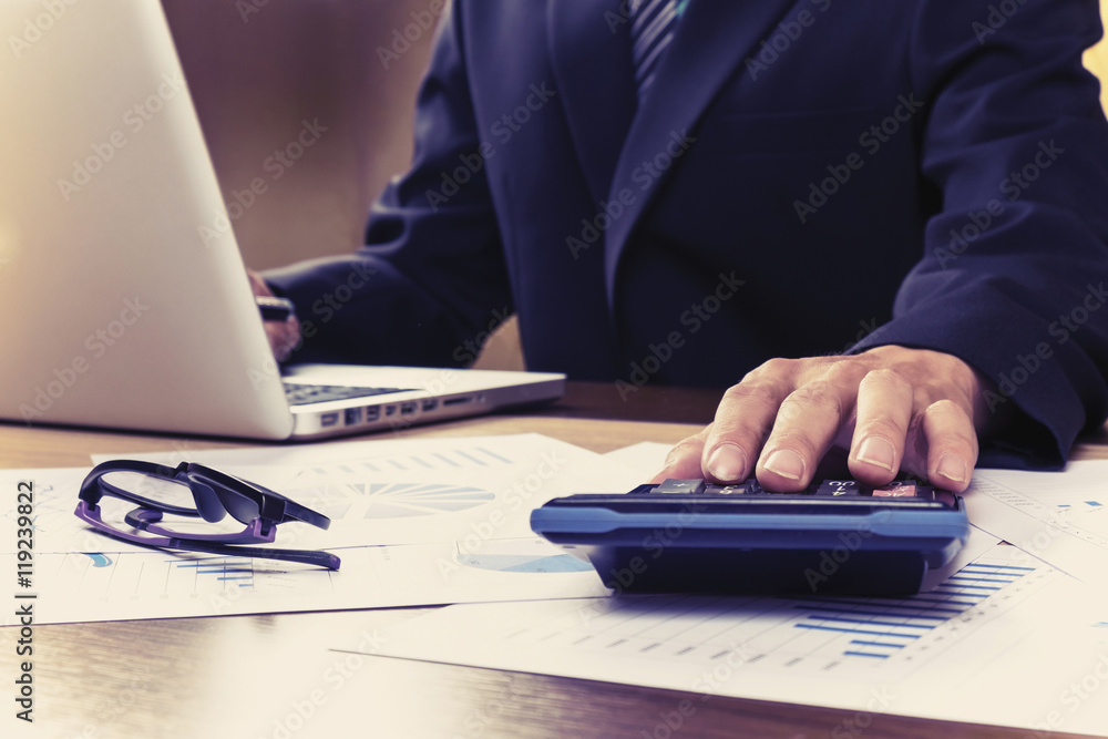 Asian Business man using a calculator to calculate the numbers.Vintage tone Asian Business man using a calculator to calculate the numbers.Vintage tone