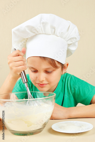 Young funny boy in chefs hat shuffles dough for baking the cake