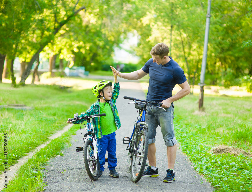 father and son give high five while cycling in the park father and son give high five while cycling in the park