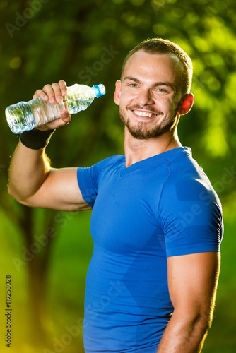 Athletic sport man drinking water from a bottle. Cold drink after outdoor fitness.