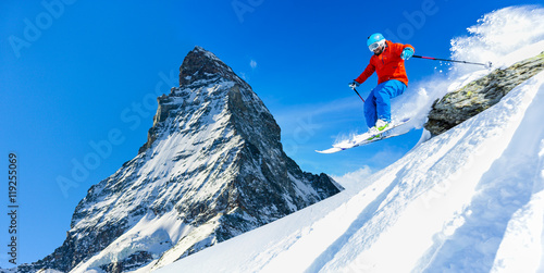 Male skier skiing in fresh snow off ski slope jumping from the rocks on a sunny winter day at high mountain in Swiss Alps. Freeski in powder snow. Matterhorn in background.