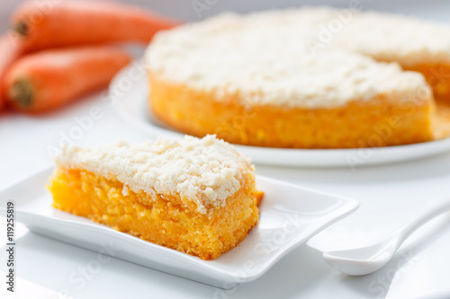 Saint-Petersburg, Russia - June 12, 2016: a slice of homemade vegan carrot cake with white crispy crumb on the white square plate. The whole cake and a few carrots on the background.
