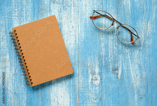 Brown notebook with glasses on blue wooden floor.