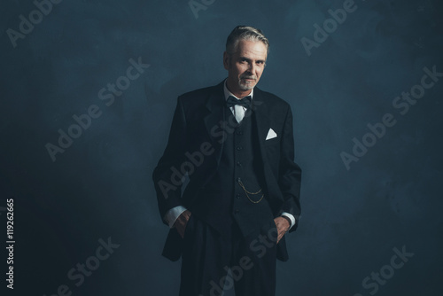 Confident middle aged retro 1920s businessman in black suit with photo