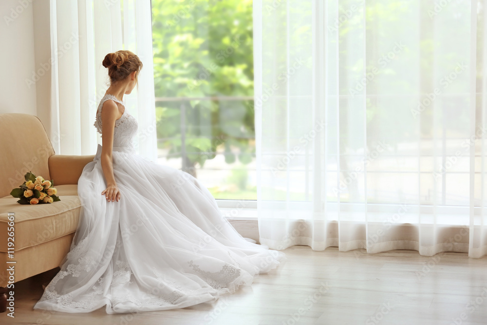 Bride in beautiful dress with wedding bouquet sitting on sofa Bride in beautiful dress with wedding bouquet sitting on sofa