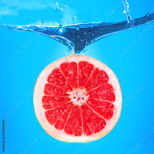 Fototapeta Naklejka Na Ścianę i Meble -  Fresh grapefruit falling in water on blue background
