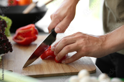 Male hands cutting red pepper on wooden board closeup