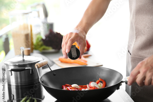 Male hand adding salt to vegetables in pan closeup