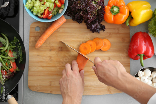 Female hands cutting carrot on wooden board, top view