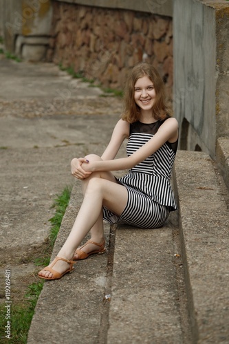 Pretty young teenage girl in striped dress sits on stairs © boomeart