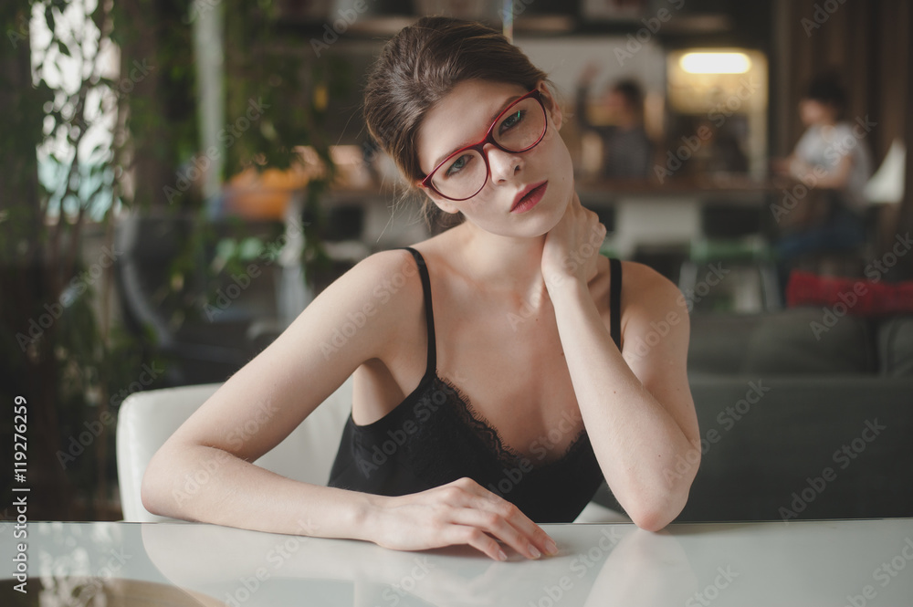Girl sits at table in red with glasses touches herself