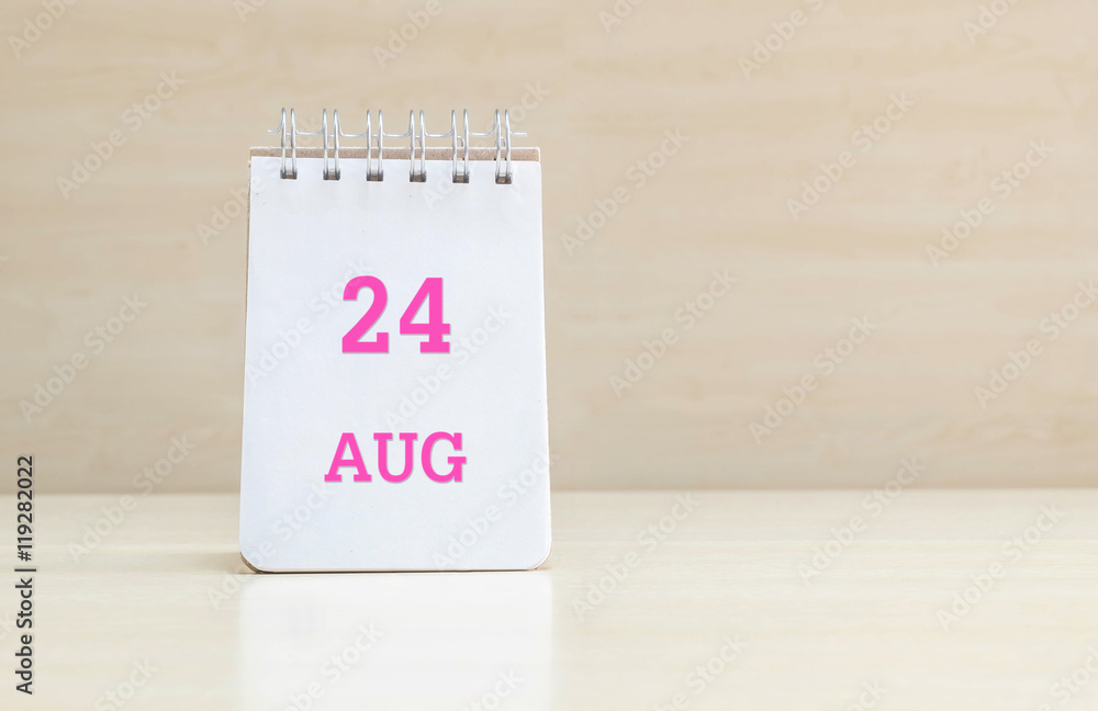 Closeup surface note book with pink 24 aug word in page on blurred brown wood desk and wood wall textured background with copy space under window light Closeup surface note book with pink 24 aug word in page on blurred brown wood desk and wood wall textured background with copy space under window light
