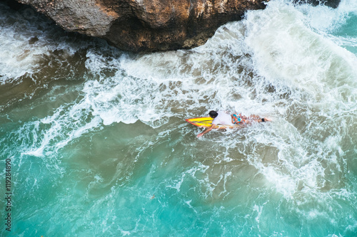Outdoors aerial view of surfer swimming on a board near huge blue ocean wave and dangerous cliff in Bali, Indonesia © moeimyazanyato
