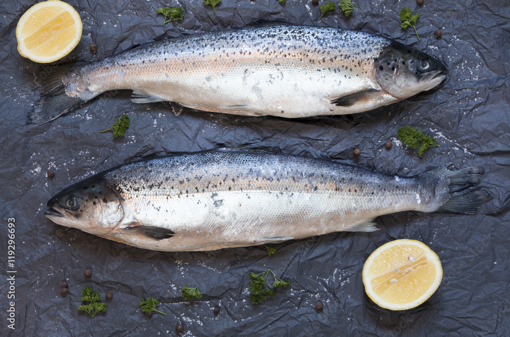 Fresh uncooked fish on black background with lemon, top view Fresh uncooked fish on black background with lemon, top view