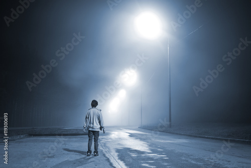 young man standing on the road in the fog near the forest. blue toning