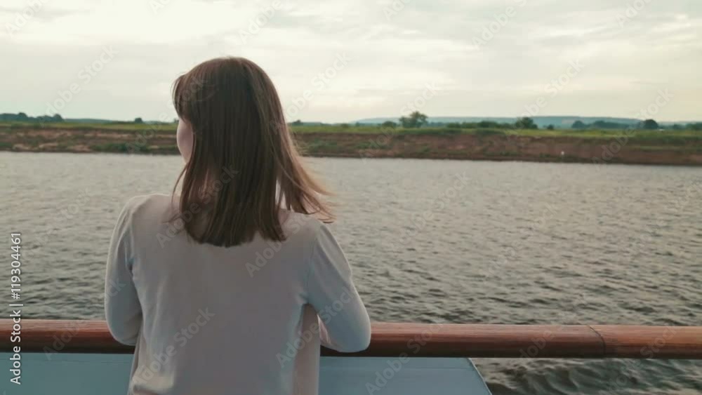 Portrait of young happy beautiful woman on deck of cruise ship. She smiling and looking at river. Rain clouds, overcast. Wind waving her hair. The river can be seen in the background behind her. Portrait of young happy beautiful woman on deck of cruise ship. She smiling and looking at river. Rain clouds, overcast. Wind waving her hair. The river can be seen in the background behind her.