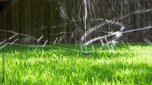 Water from a backyard sprinkler twirls and spins around in dance like fashion bathed in afternoon sunlight. Slow motion footage. photo