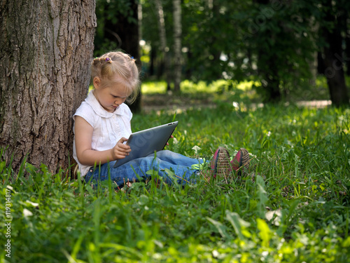 Child with tablet pc outdoors. Little girl on the grass with a computer