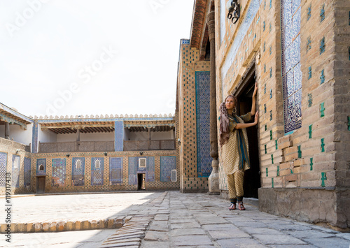 Young woman in Central Asia, in Uzbekistan the national dress, standing against a wall in the courtyard of the madrasah, the city of Khiva. © razoomanetu