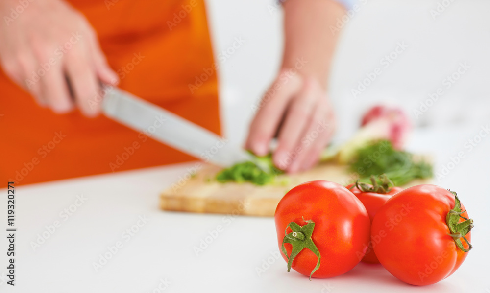 Healthy eating, vegetarian food, cooking, dieting and people concept. Three ripe tomatoes with a man cutting ripe vegetables on a wooden board on the background.