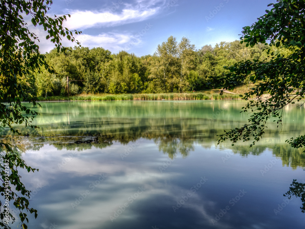 Hydrogen sulphide lake landscape with turquoise water in tree branches framing with forest reflection.