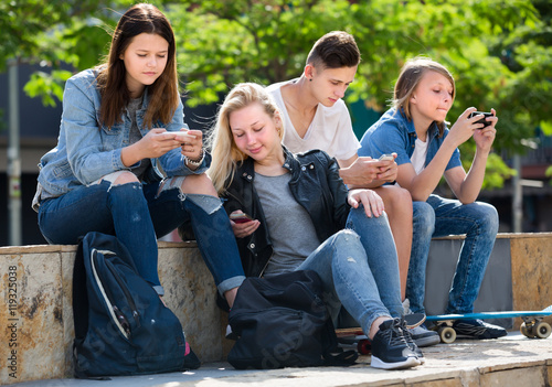 Smiling teenagers playing with mobile phones