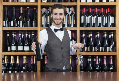 Bartender Holding Red Wine Bottle And Glass In Shop