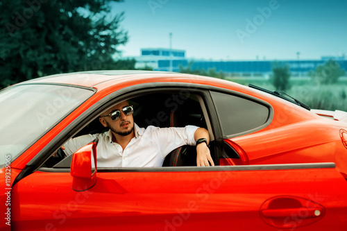 stylish man in sunglasses in red sport car
