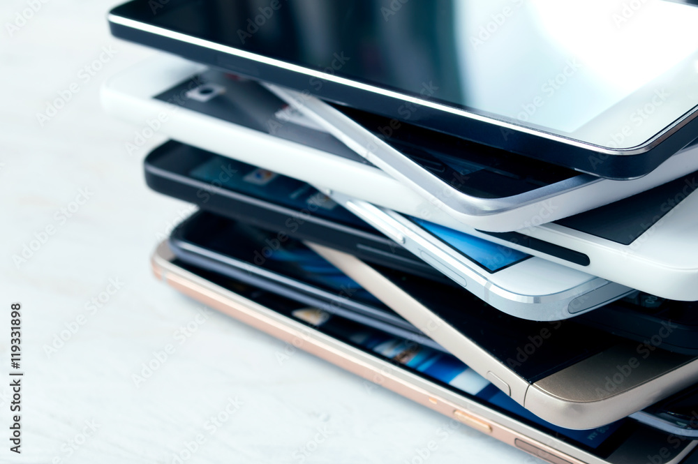 Stack of high-end smartphones on white wooden desk Stack of high-end smartphones on white wooden desk