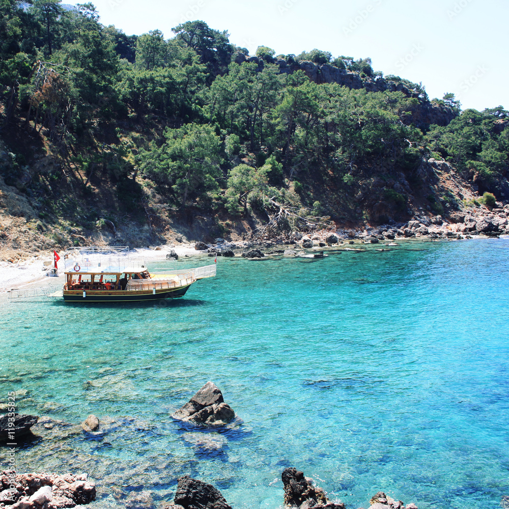 Tourist boat in the small bay. Calm blue sea and green hills in Turkey. Passenger vessel waiting for tourists. Aged photo. Walking the Turkey's Lycian Way. Wide photo for web site slider.