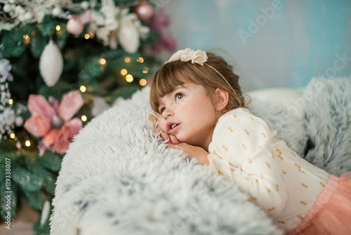 The little girl looks dreamily on the tree in anticipation of holiday