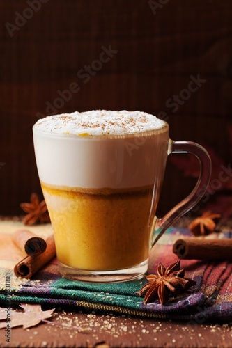 Pumpkin spiced latte or coffee in a glass on a wooden table. Autumn or winter hot drink.