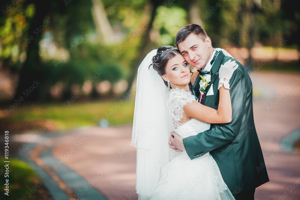 Handsome groom hugging beautiful bride with bouquet in romantic european park