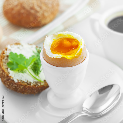 Perfect soft boiled egg, open bread sandwich with butter and cup of coffee on a table. Traditional food for healthy breakfast.