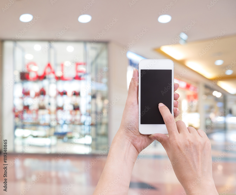 Hands holding mobile phone with blurred image of shopping mall Hands holding mobile phone with blurred image of shopping mall