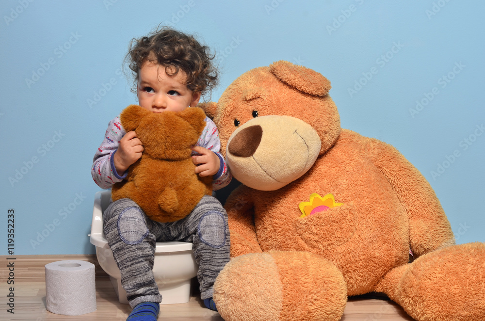 Baby toddler sitting on a potty surrounded by teddy bears. Cute kid