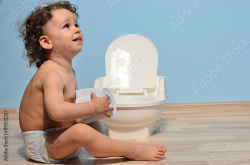 Baby toddler sitting near the potty and playing with toilet paper. Cute kid potty training for pee and poo