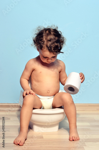 Baby toddler sitting on the potty and playing with toilet paper. Cute kid potty training for pee and poo