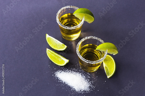 Gold tequila with lime and salt on dark table