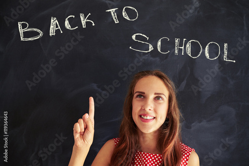 Close-up of charming smiling schoolgirl pointing at back to scho photo