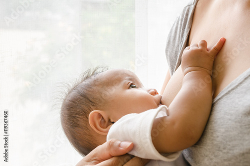 Mother breastfeeding her newborn baby beside window