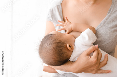 Mother breastfeeding her newborn baby beside window photo
